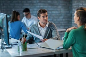 male entrepreneur discussing about business reports with female colleague while working office desk there are people background 637285 1039 male entrepreneur discussing about business reports with female colleague while working office desk there are people background 637285 1039